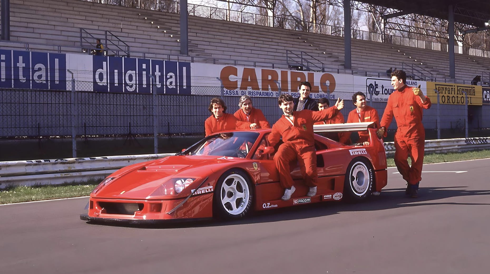 Team in tuta rossa in posa sulla Ferrari F40 Competizione con sponsor Pirelli al circuito di Monza